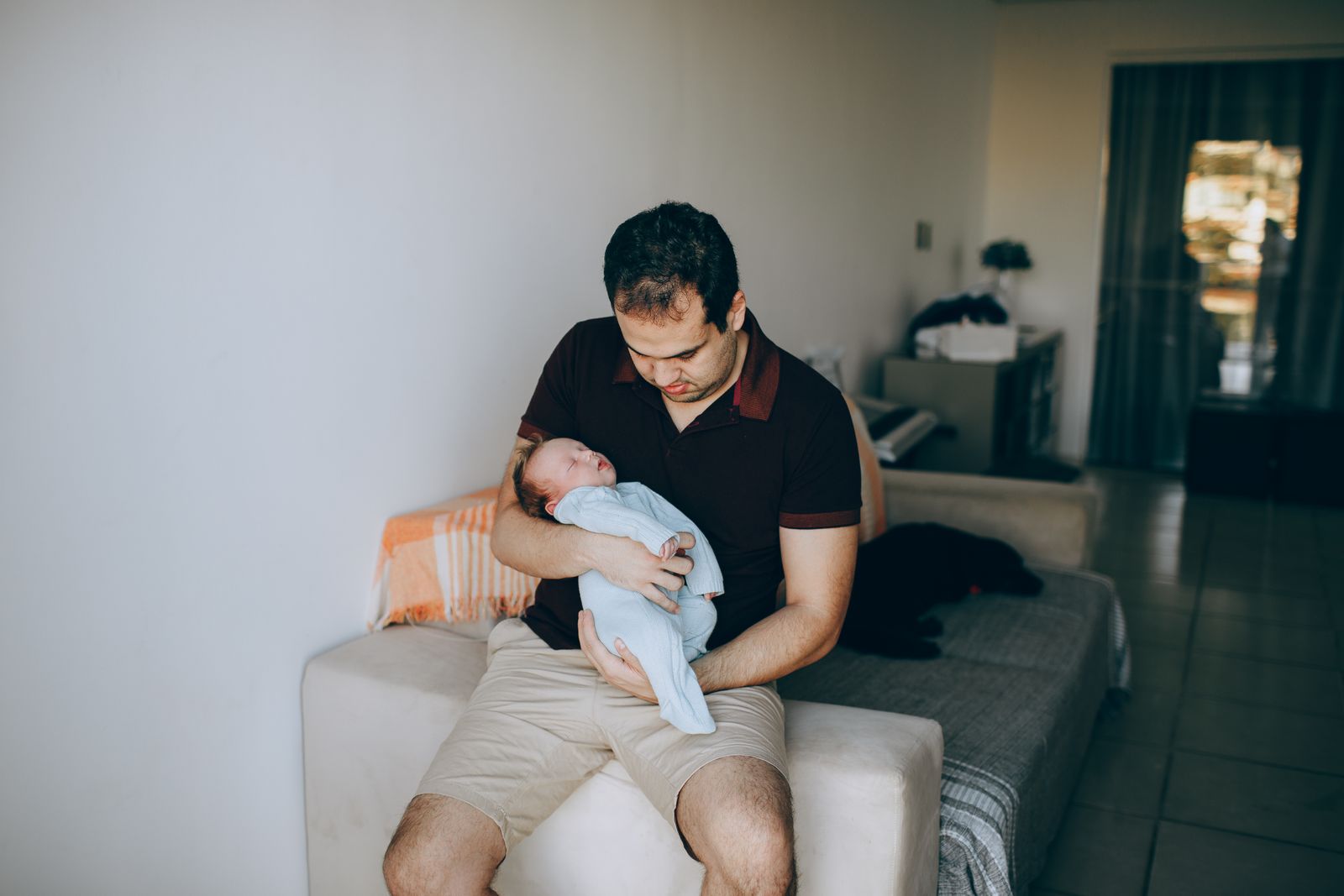 A father holding a sleeping newborn on a couch