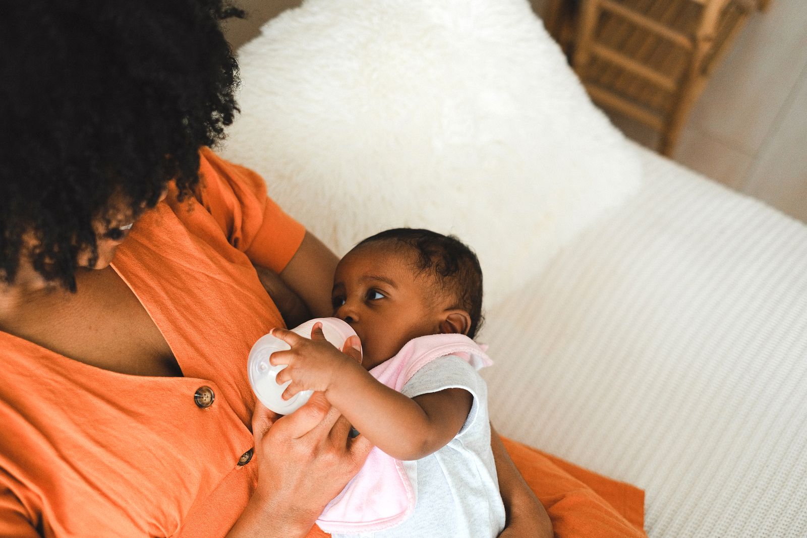 A mother in an orange top feeding her baby a bottle