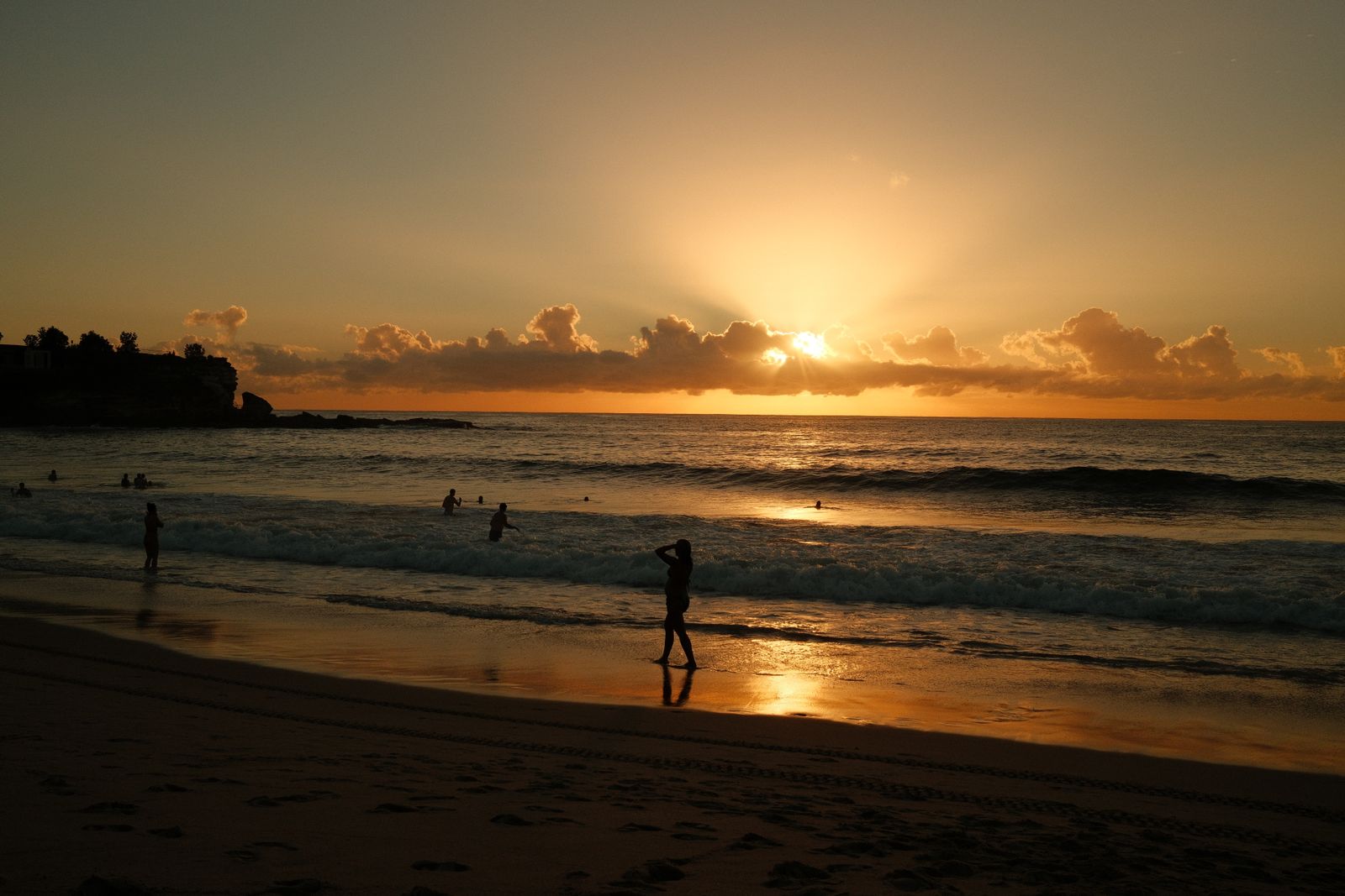 Sunrise over Bondi Beach in Sydney with a few people walking the shoreline