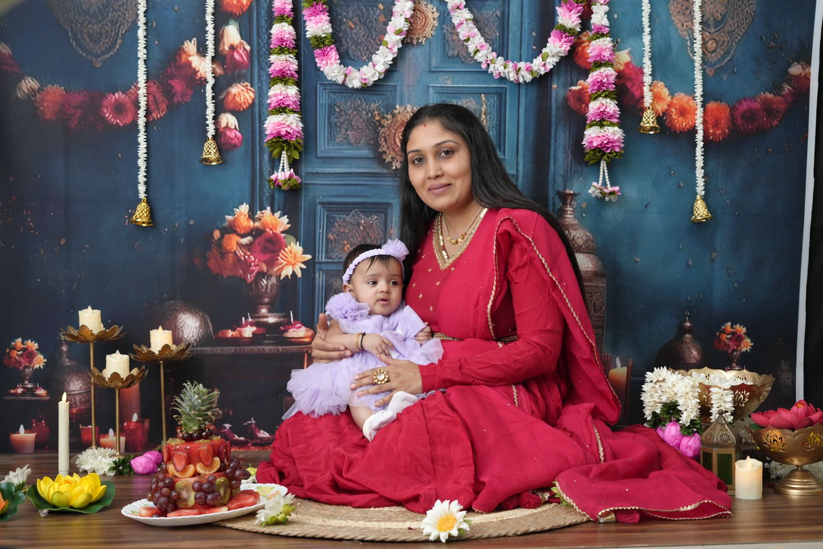 A mother in a red kurta sitting with her baby among marigold garlands and flowers