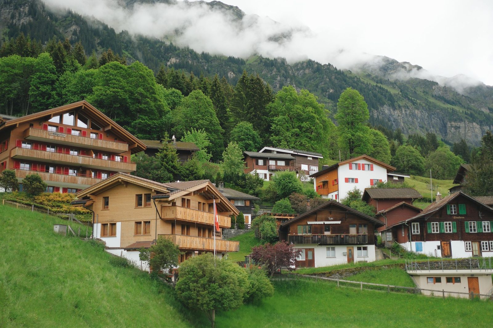 Wooden chalets on a green hillside below misty mountains in Lungern, Switzerland