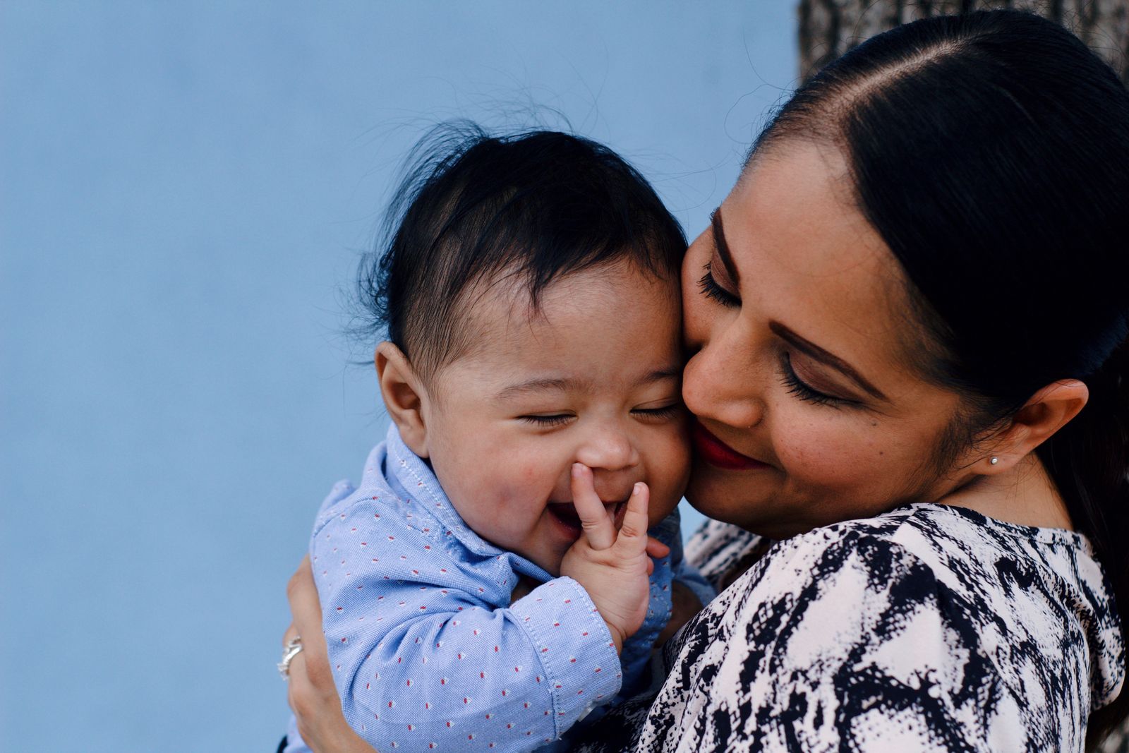 A smiling mother holding her laughing baby cheek to cheek