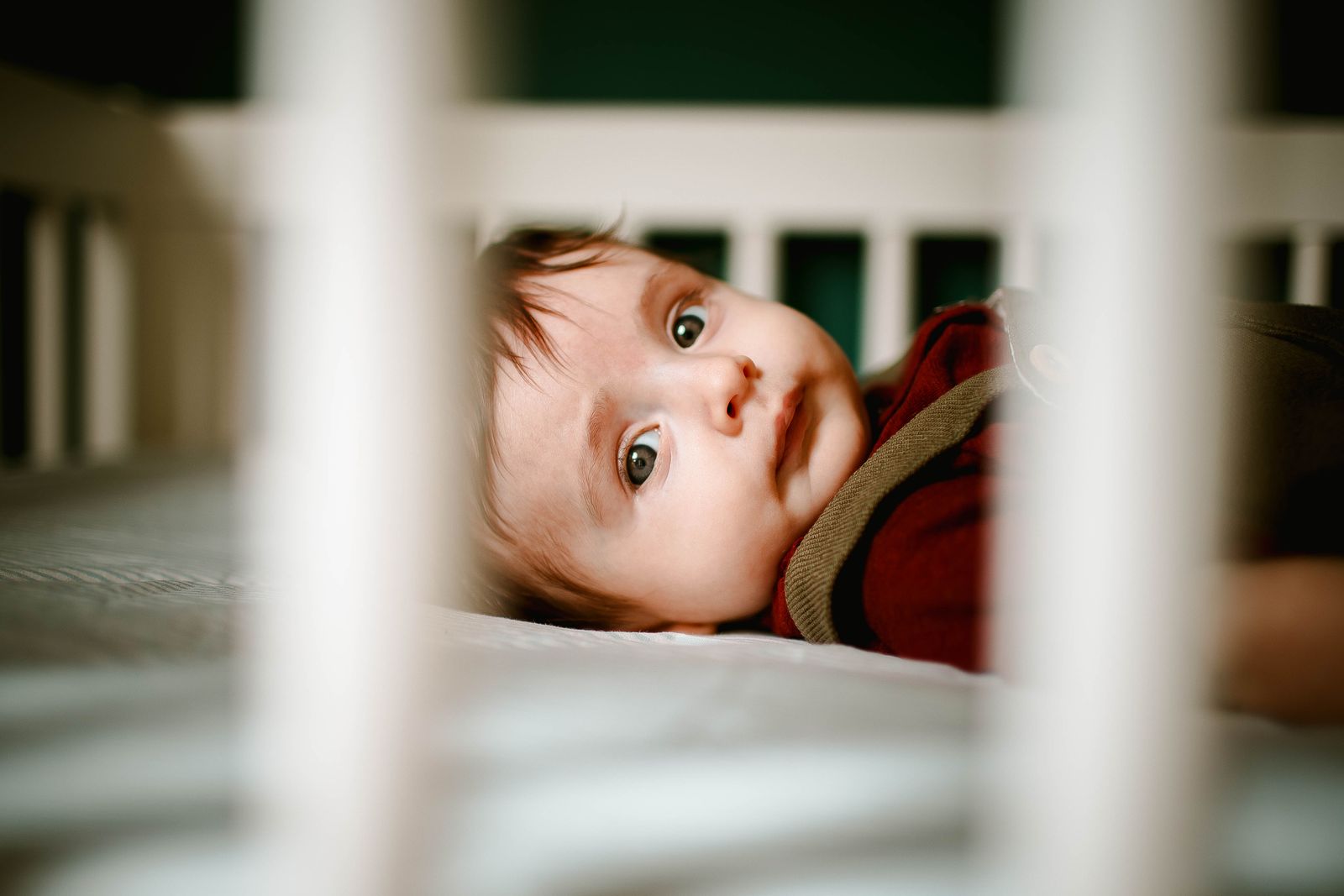 A peaceful baby gazing out between crib bars