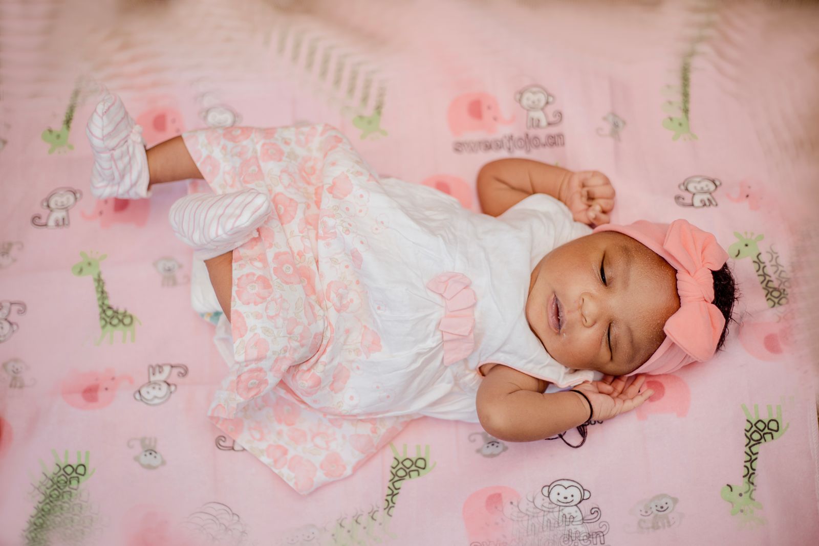 A sleeping baby in a pink bow on a pink blanket