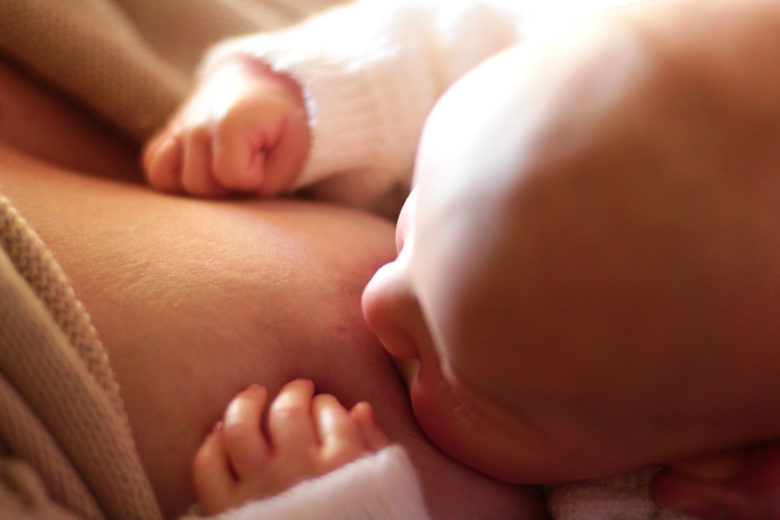 A newborn's face and tiny fist close up while nursing in warm light