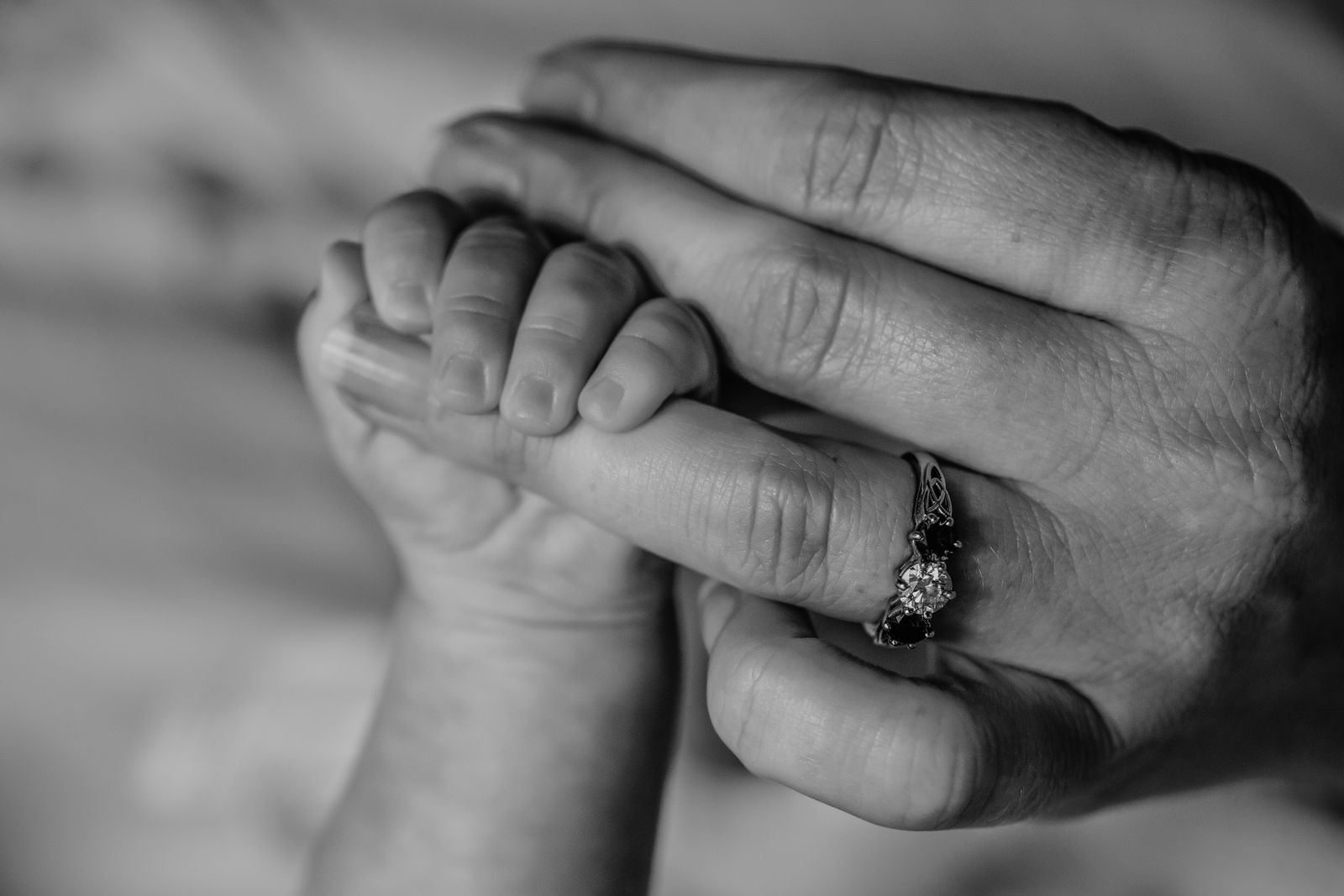 A black and white close-up of a baby's hand gripping a mother's finger
