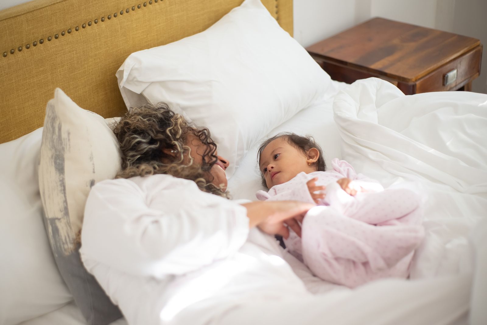 A mother and baby girl lying face to face in white bedding