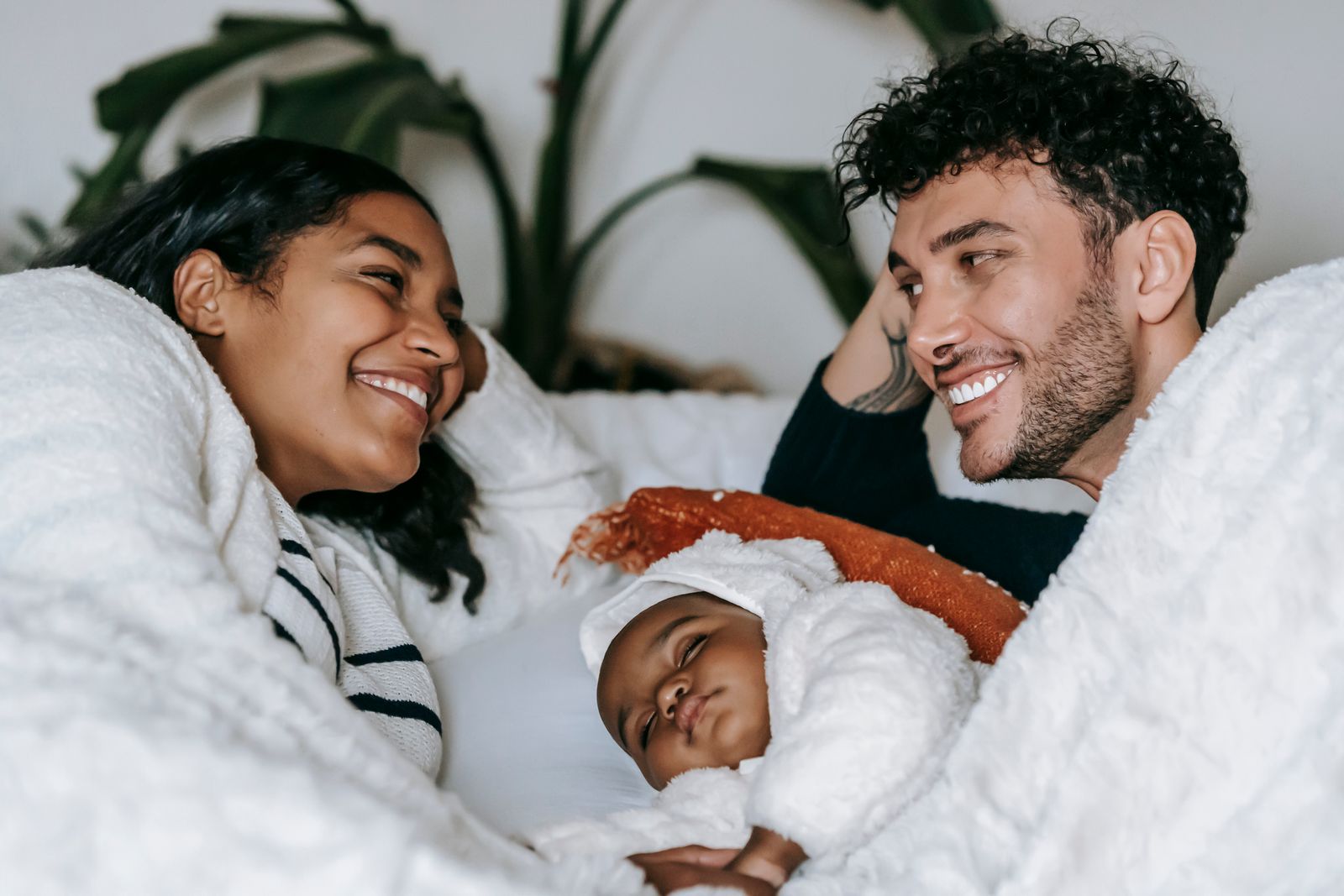 Two parents smiling over their sleeping baby on a bed