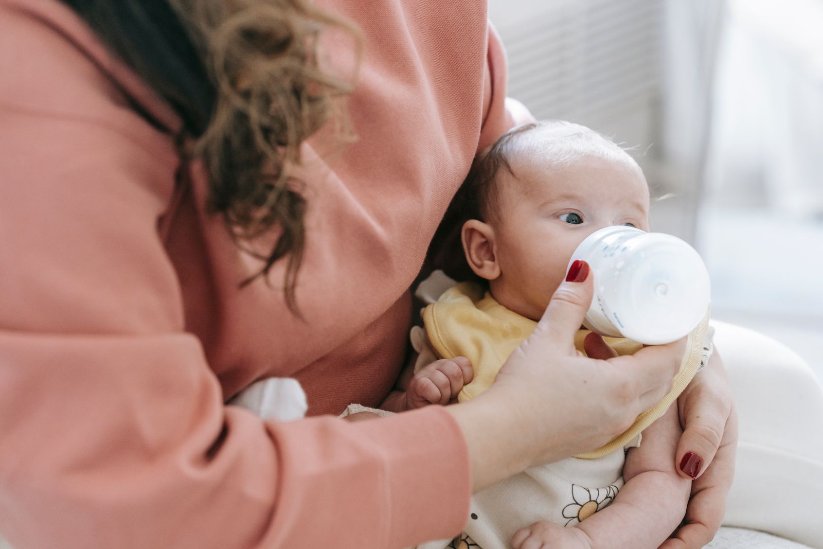 A mother cradling her young baby in one arm while giving a bottle
