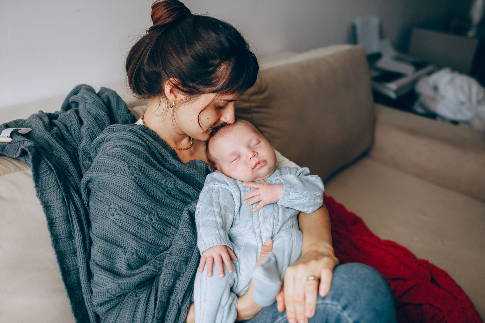 A mother kissing the head of her sleeping baby on a sofa